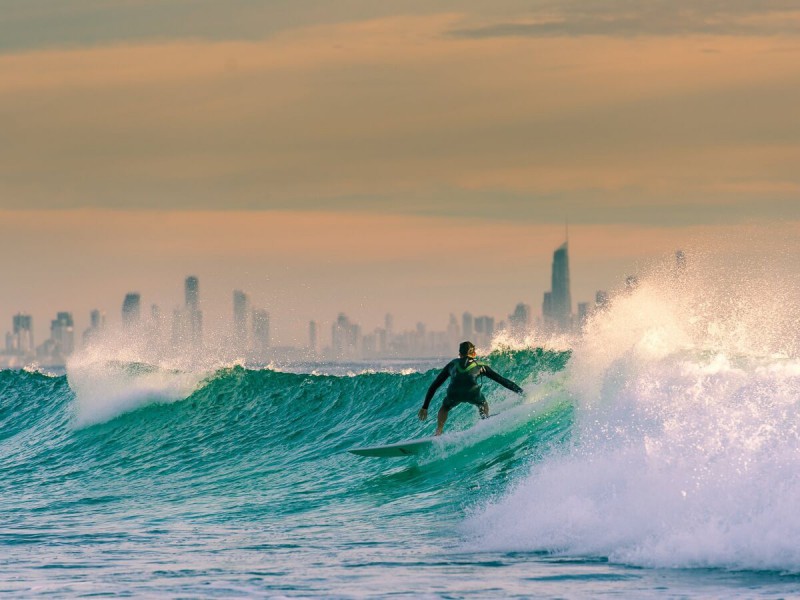 Surfař na vlně a v pozadí panorama mrakodrapů Gold Coast v Austrálii.