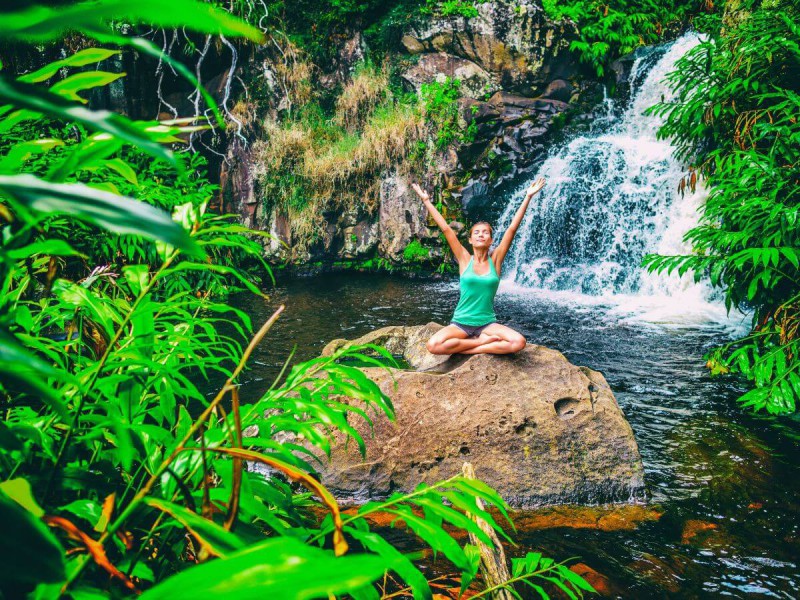 Žena v jogínské pozici u vodopádu si užívá přírody na Kauai na Havaji.