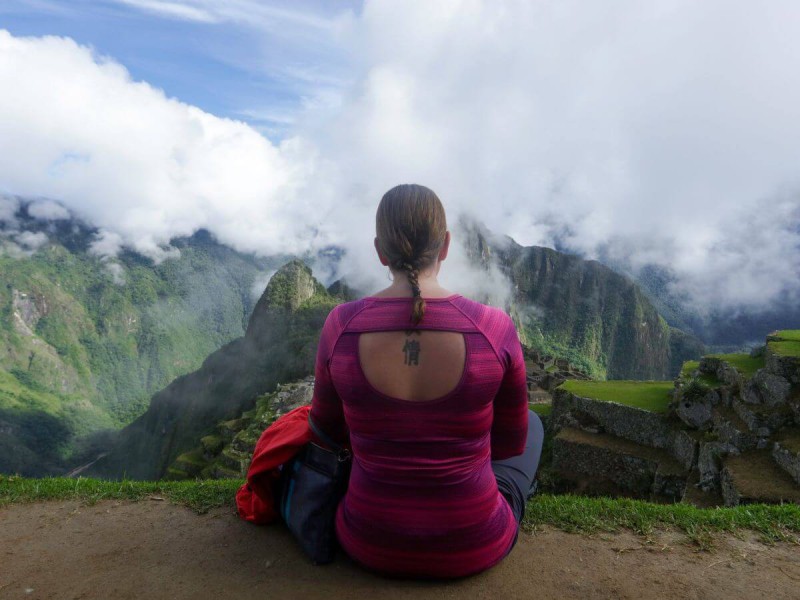 Pohled na ženu zezadu sedící v tureckém sedu, v pozadí Machu Picchu, Peru.