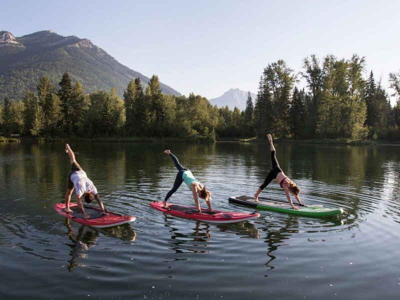 Tři lidé cvičící jógu na paddleboardu na jezeře v horách.