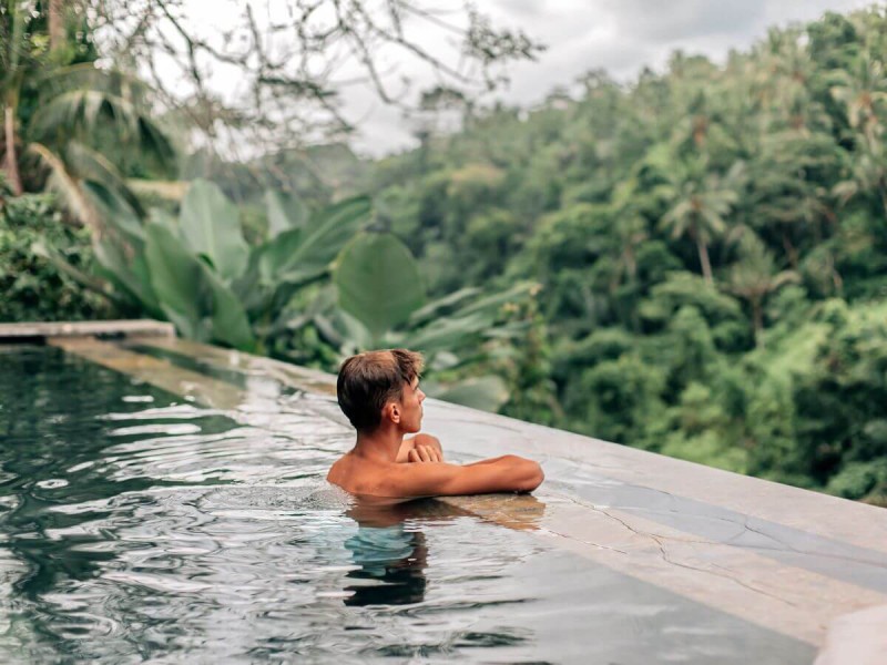 Muž v bazénu dívající se na výhled do pralesa v Ubudu na Bali.