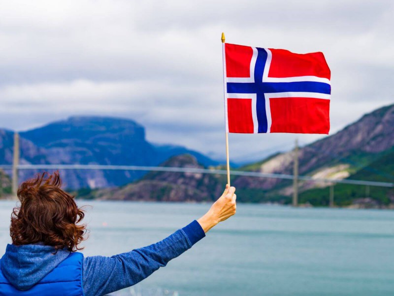 Žena s norskou vlajkou u fjordu Lysefjord.